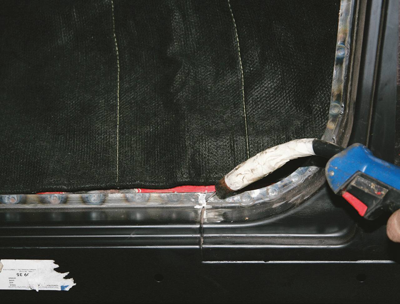 A person is applying sealant with a caulking gun to the edges of a car window to seal it.