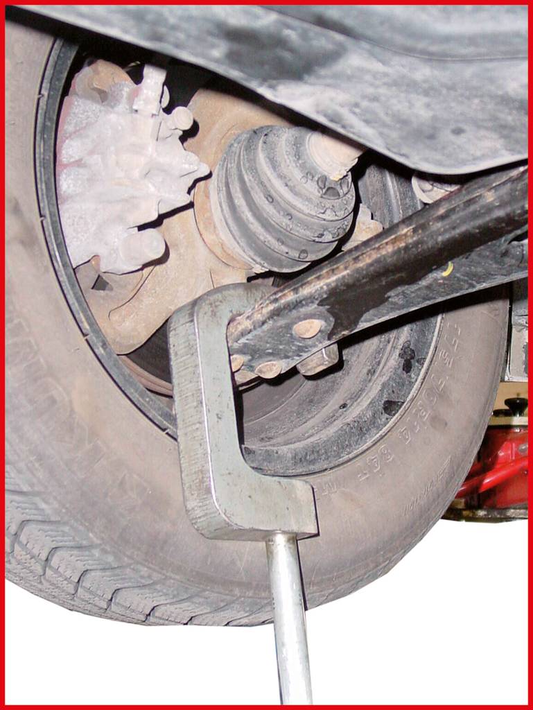 A tyre is jacked up by a tool or lever to expose the suspension and brakes.