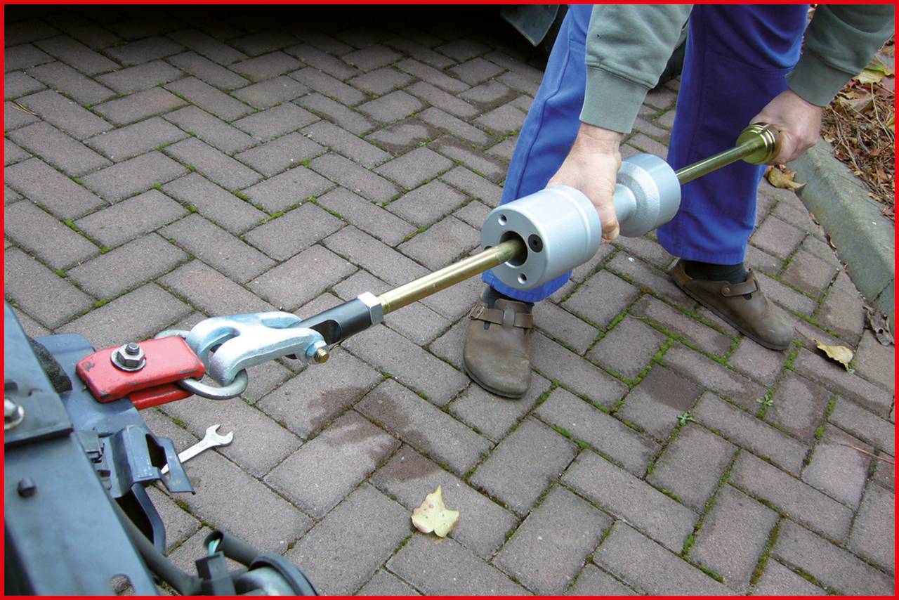 A person is using a recovery tool on a towing coupling on a paved surface.