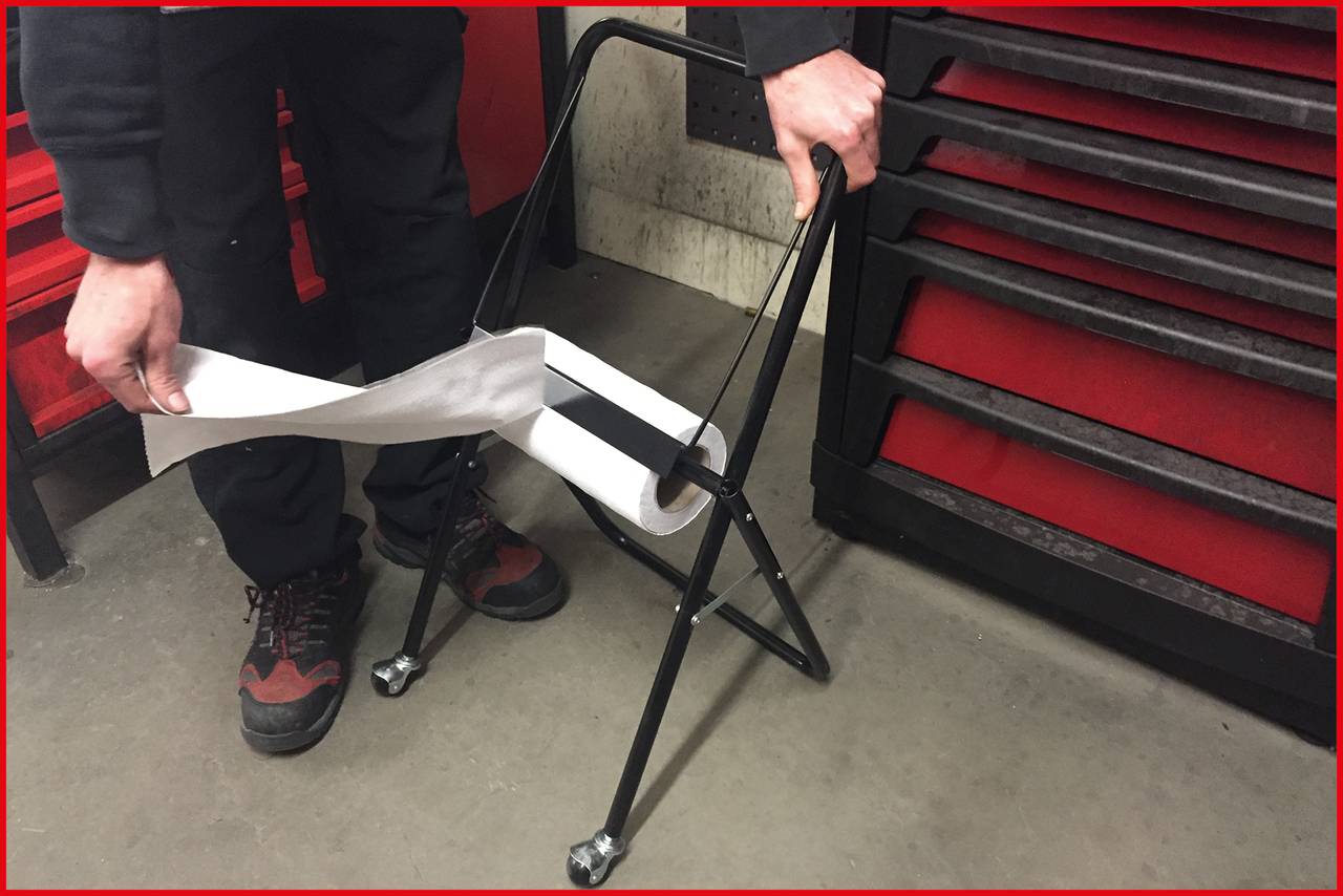 A person pulls paper from a black metal trolley with wheels. A red toolbox stands to the left.