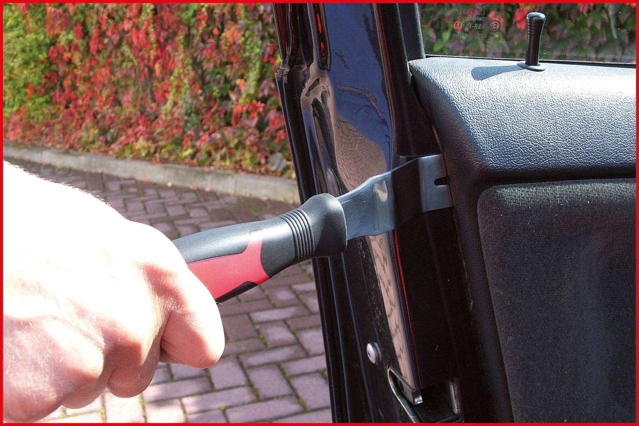 A hand is gripping a crowbar inserted into a car door, suggesting an attempted break-in. Plants can be seen in the background.