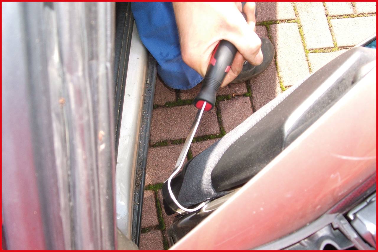 'Person uses screwdriver to lever open car door; potential attempted break-in depicted.'