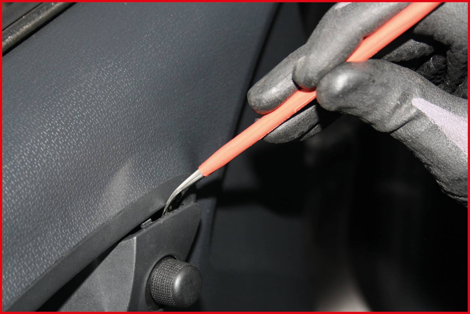 A person is using an orange tool to carefully remove a car part. Hands are wearing gloves for protection.