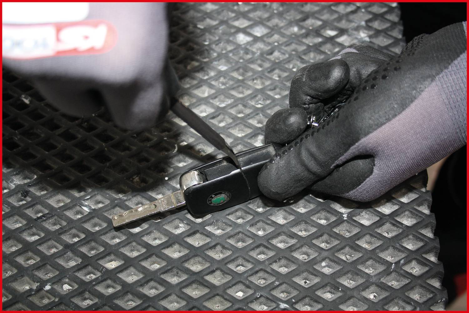 A person wearing gloves repairs a car key with a tool against a metallic background.