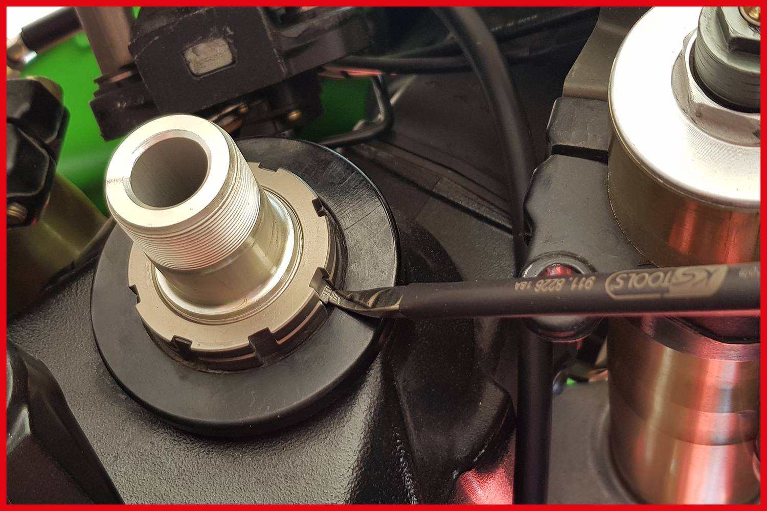 Close-up of a motorcycle transmission. A tool is being used to loosen a screw on a metal cylinder.