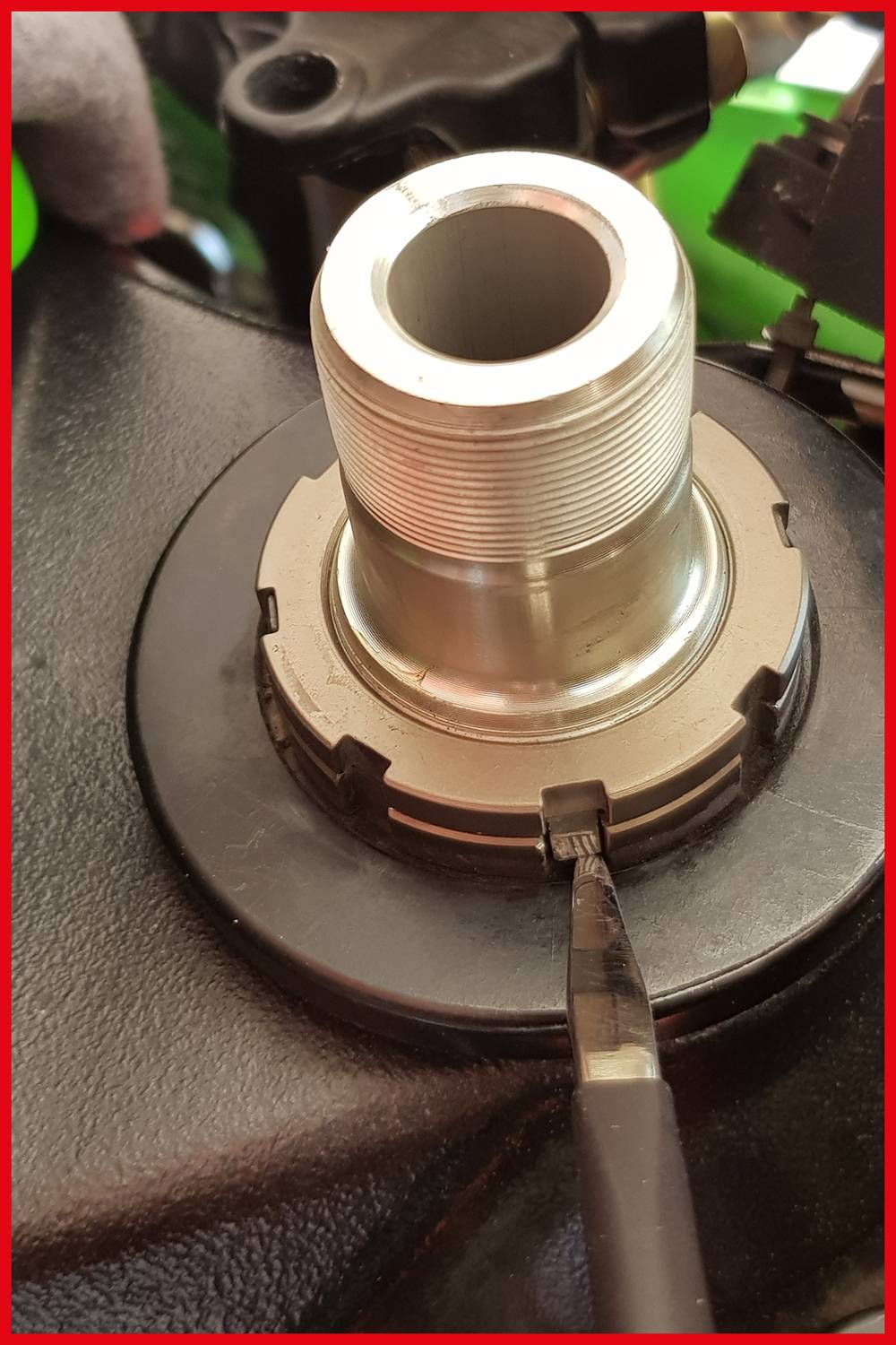 Close-up of a metallic component, likely a screw or axle, in a mechanism, surrounded by a black seal.