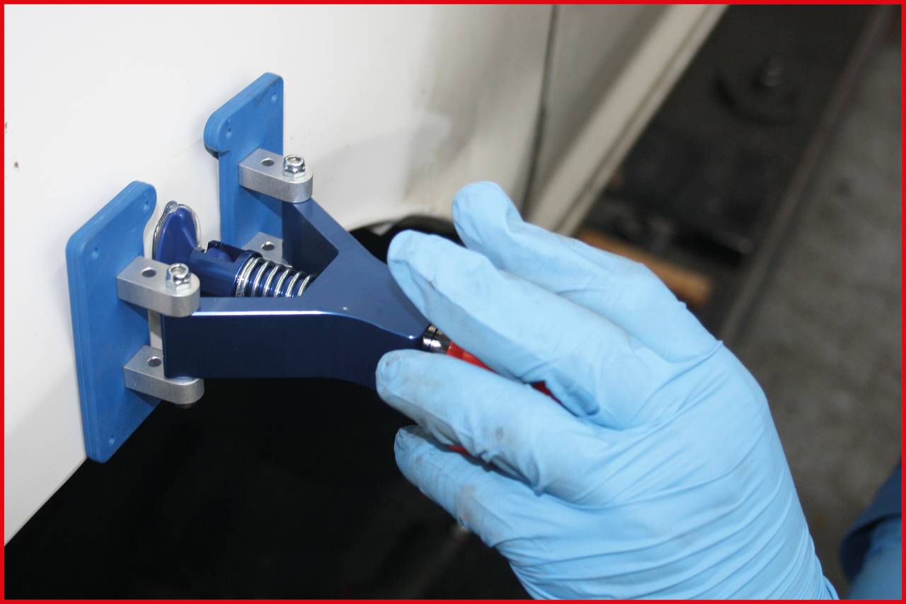 'A person wearing blue gloves is repairing a car body with a dent removal tool. The tool is secured on a blue pad.'