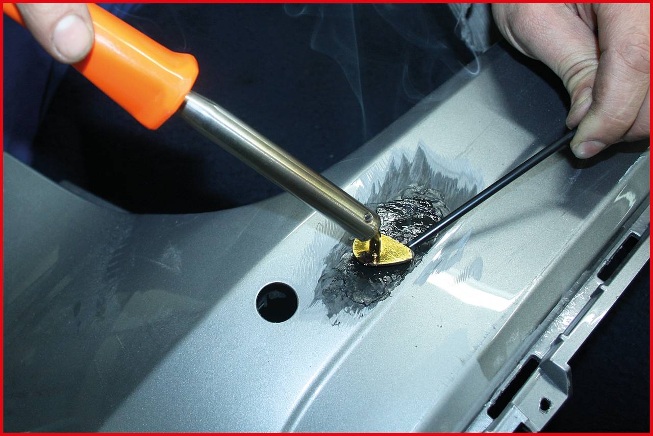 A person is welding plastic with a soldering iron on a grey surface. Smoke rises as the hands guide the tool.