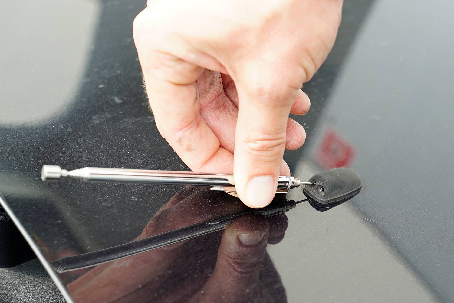 A hand holds a tyre pressure gauge on the reflective surface of a car to check the tyre pressure.
