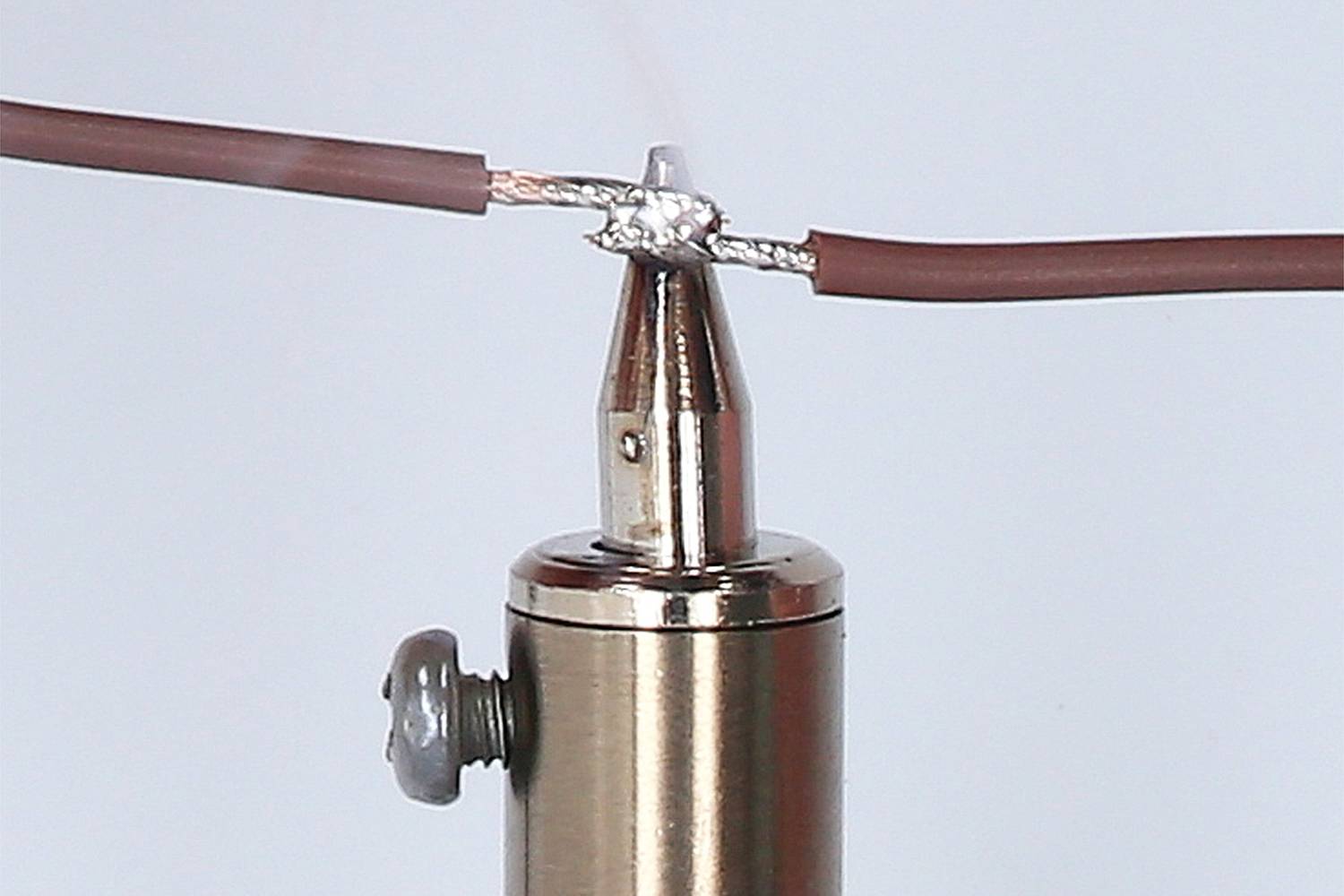 A soldering iron with a soldering tip connects two brown wires by melting solder. Electronics repair or assembly.