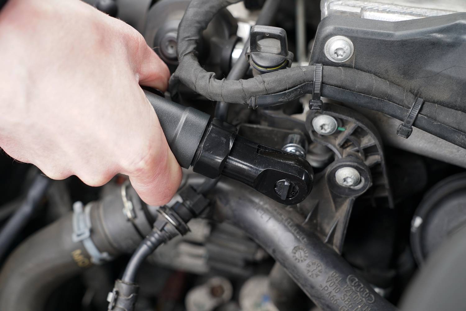 'Hand tightening a screw with a ratchet on a car engine. Close-up of the engine compartment with visible cables and mechanical parts.'