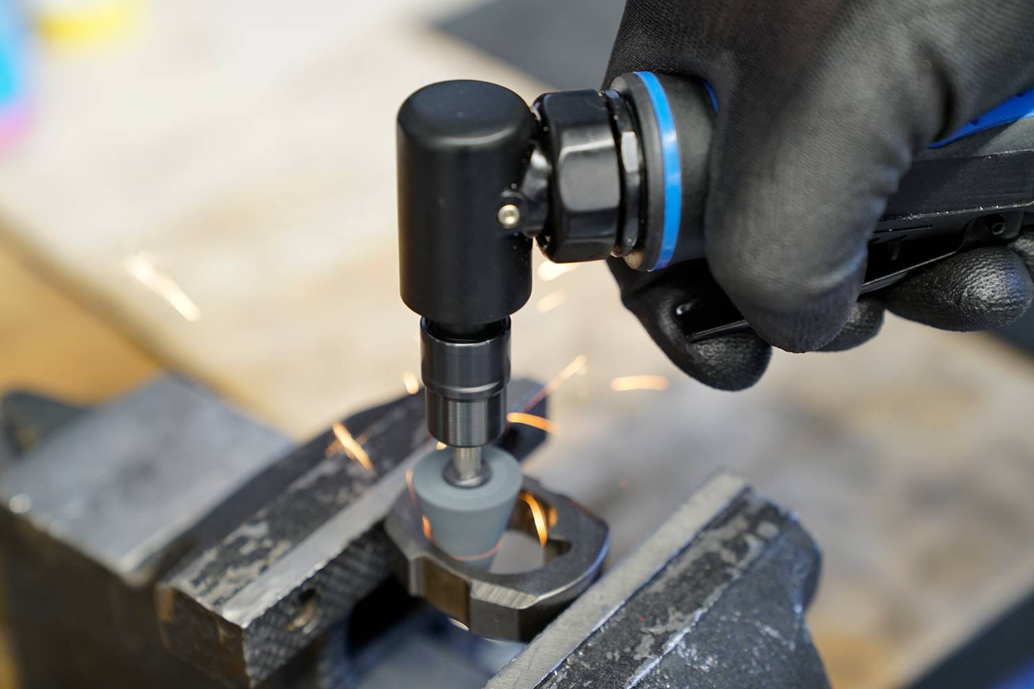 'A handheld grinding tool is working on a metal piece in a vice, while sparks are flying. The user is wearing black gloves.'