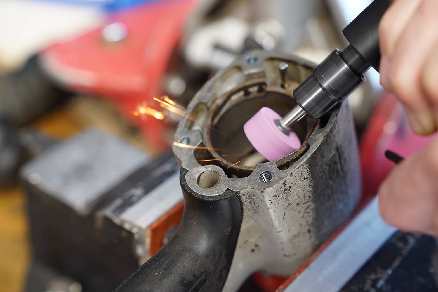 A person is grinding a metal part with a rotating tool. Sparks are flying from the point of contact.