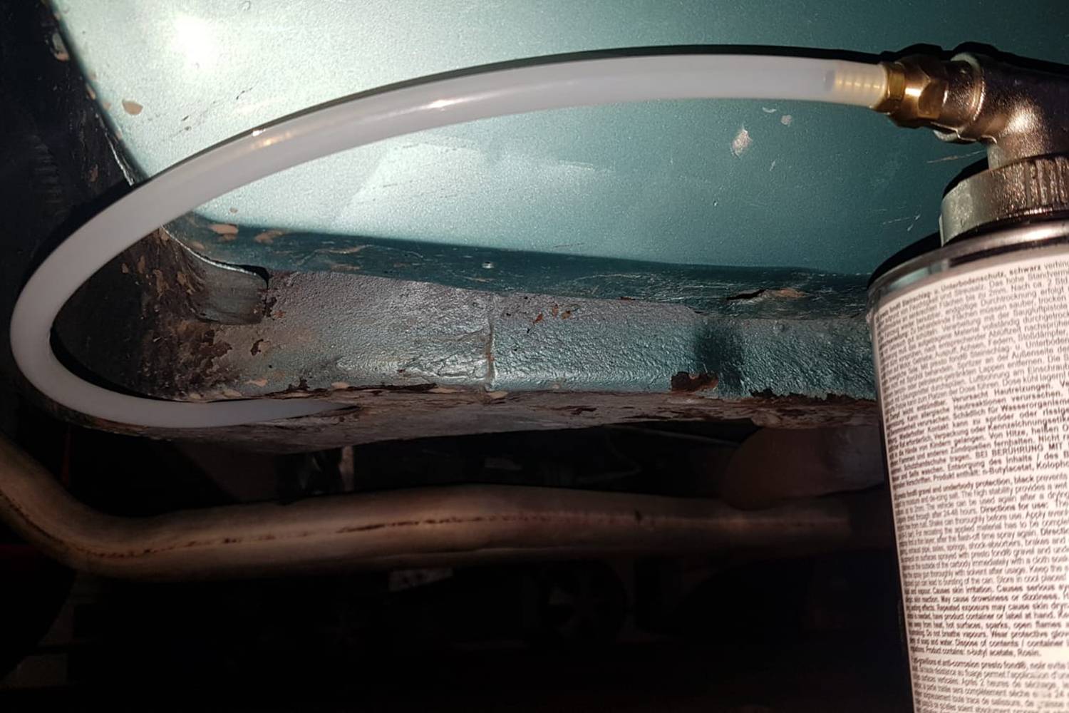 A spray hose is attached to a metal surface of a car to potentially apply rust protection.