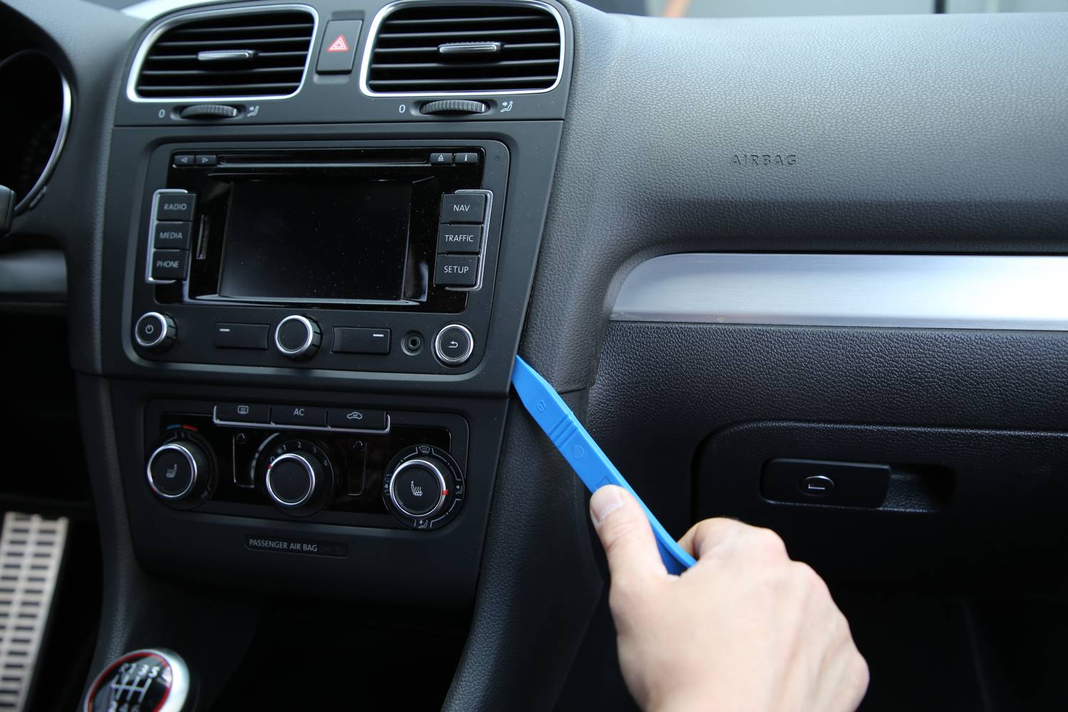 A hand is using a blue tool to remove the trim next to the car radio in a vehicle.