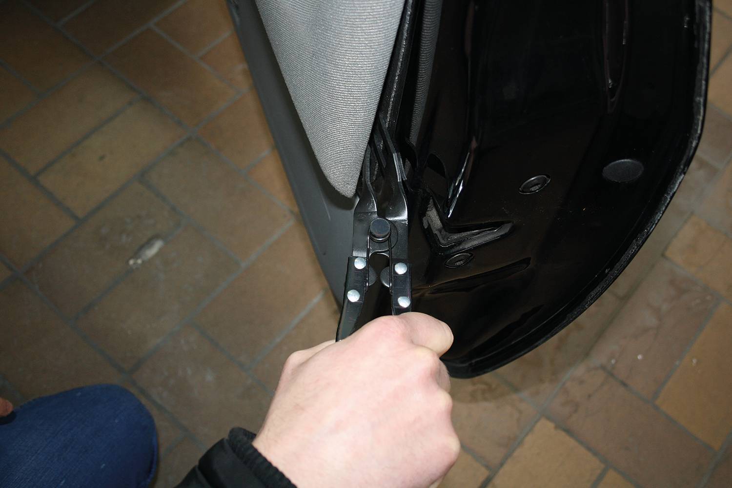 A hand is holding pliers and securing a car door seal.