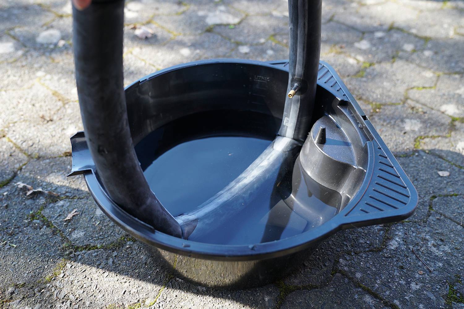 Black plastic bowl with water, two bicycle inner tubes being tested to identify leaks, outdoor use on cobblestones.