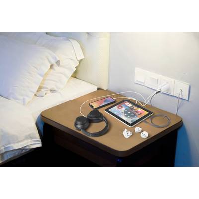 Bedside table with headphones, tablet, smartphone and charger. The tablet displays apps. Two power sockets are on the wall.