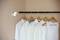 Five light-coloured shirts and a vest top hang on wooden coat hangers from a black rail. A small, bright lamp is positioned to the left.