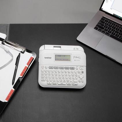 A laptop, a label printer and a clipboard with a pen are lying on a black table. They convey an office or work environment.