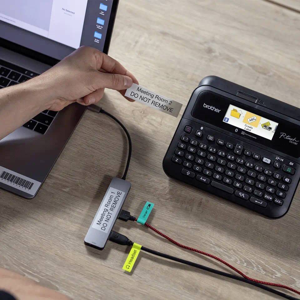 A hand is holding a labelled tag with the inscription 'Meeting Room 2 - DO NOT REMOVE'. A label printer is visible in the background.