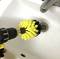 Cordless drill with brush attachment cleans a sink. Yellow and black brush rotates to remove dirt and grime.