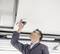 A man in workwear is examining or installing a surveillance camera on the ceiling in a modern building.
