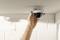 A hand is mounting a surveillance camera on a white ceiling in a room with white walls.