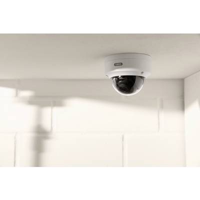 Security camera mounted on the ceiling of a bright room, pointing towards a corner with white brick walls.