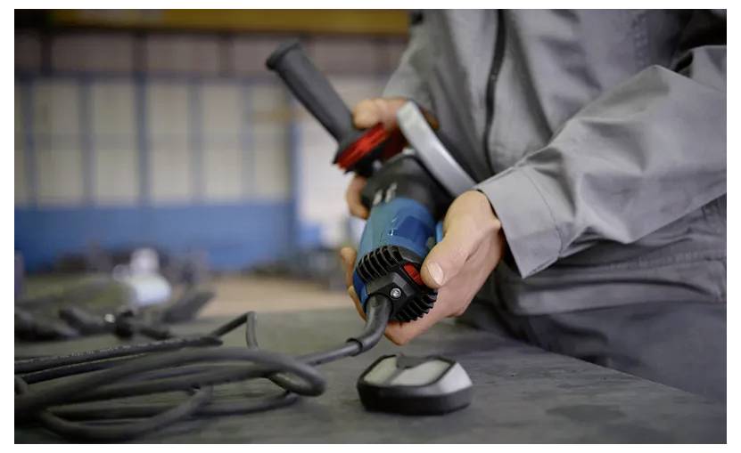 Person holding a power tool with a cord, preparing for use on a workbench in a workshop environment.