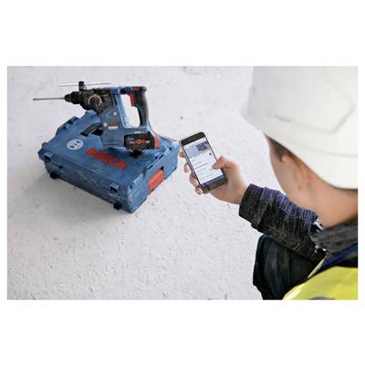 A person using a smartphone to control or monitor a Bosch power tool placed on the floor. The tool is in a blue carrying case.