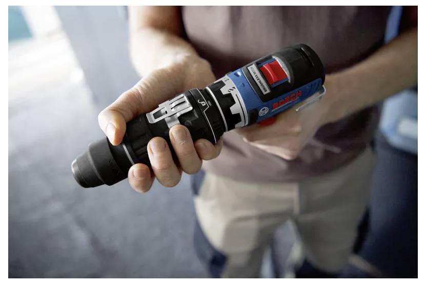 'A person holds a cordless power drill featuring a blue and black design, with a red button and visible product branding.'