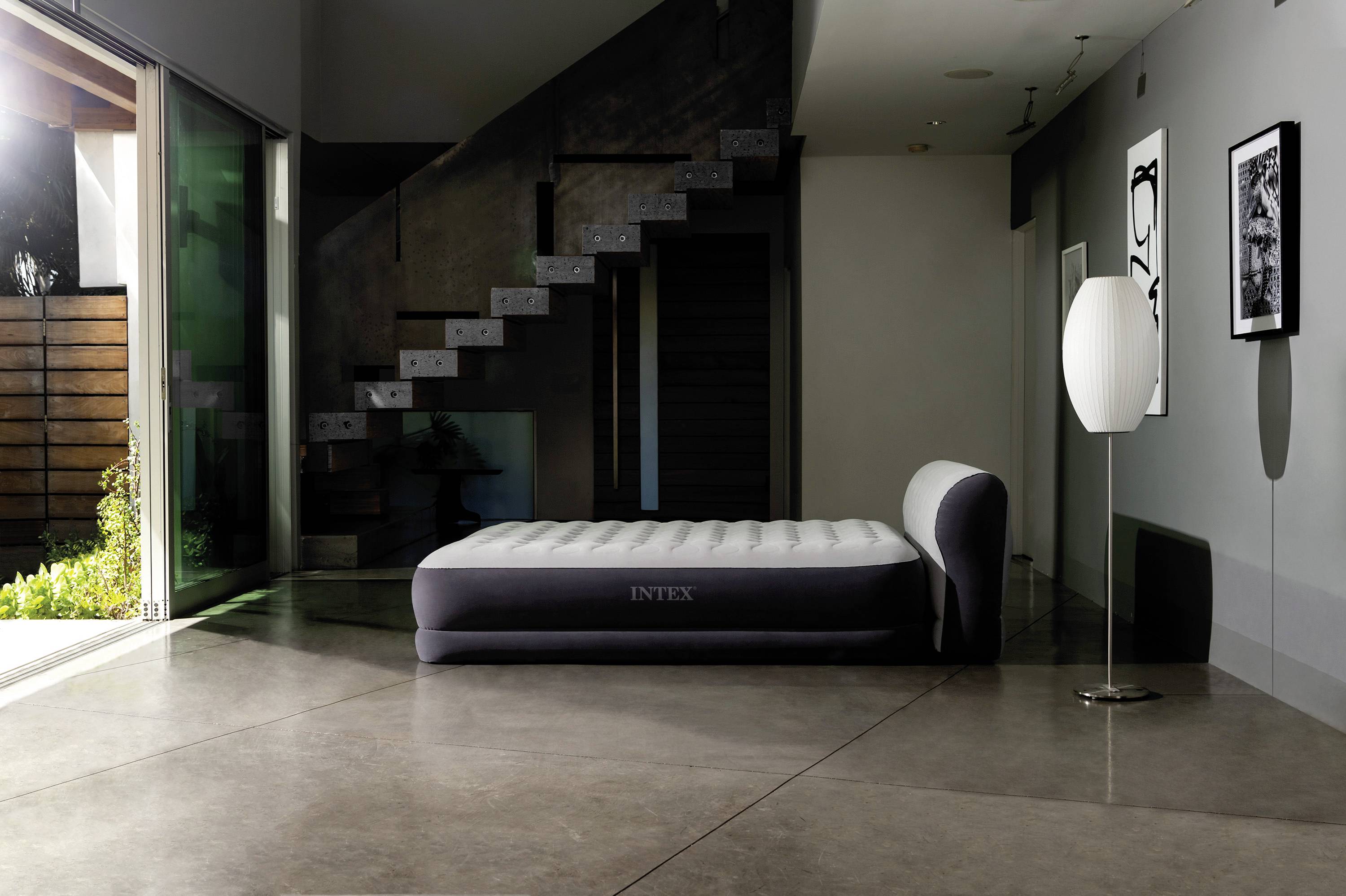 Air mattress in a modern living room with stairs in the background. Daylight from the left. Minimally furnished.