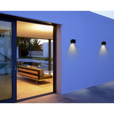 A contemporary lounge with illuminated interior and a large window offering a view of a terrace with a swimming pool and palm trees.
