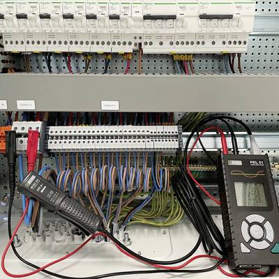 An open electrical cabinet with multiple fuses and cables. On the right is a digital meter displaying energy consumption.