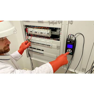 An electrician wearing a safety helmet and protective gloves is conducting a measurement on an open electrical distribution board using a measuring device.