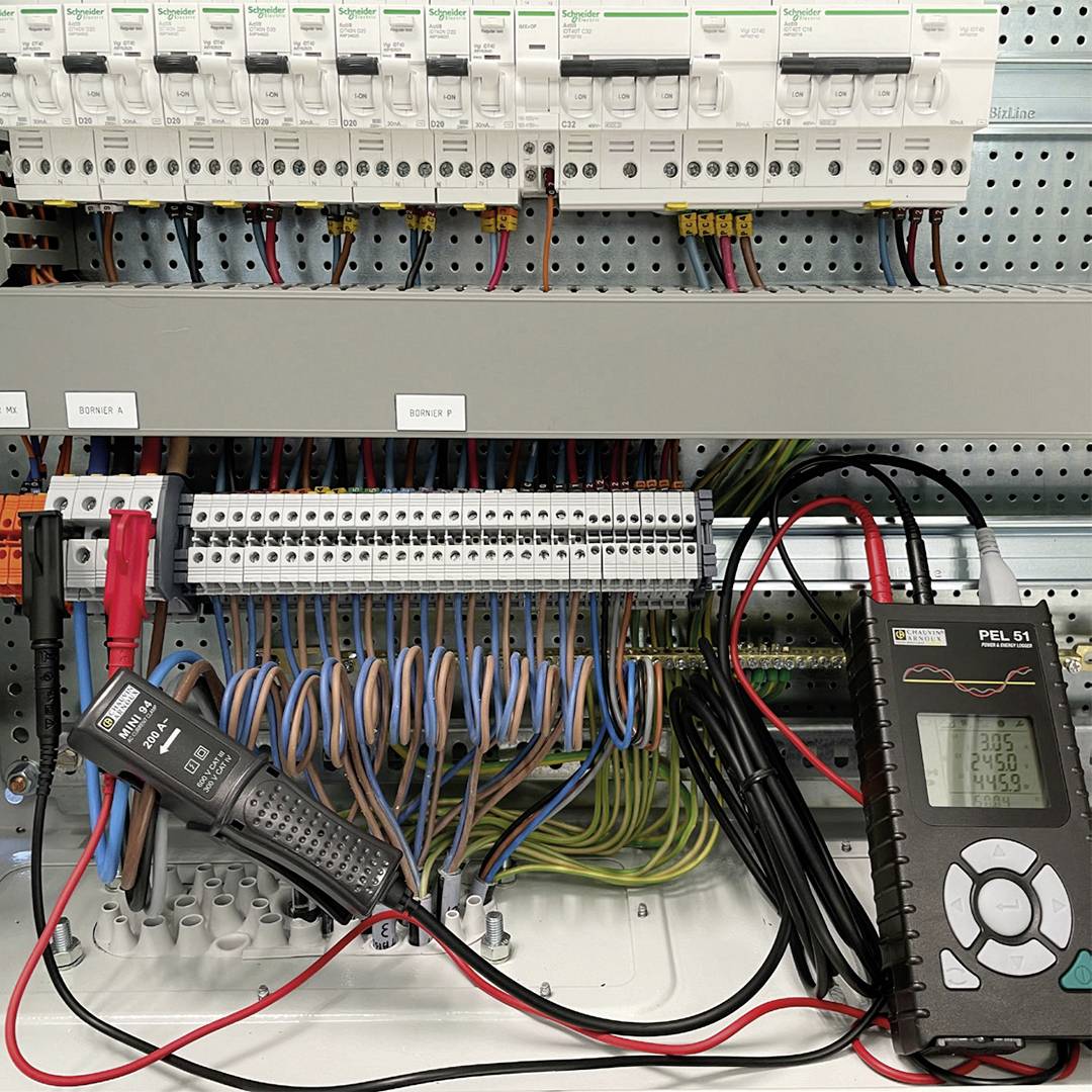 An electrical control cabinet with multiple circuit breakers and wiring. A measuring device displays electrical values.