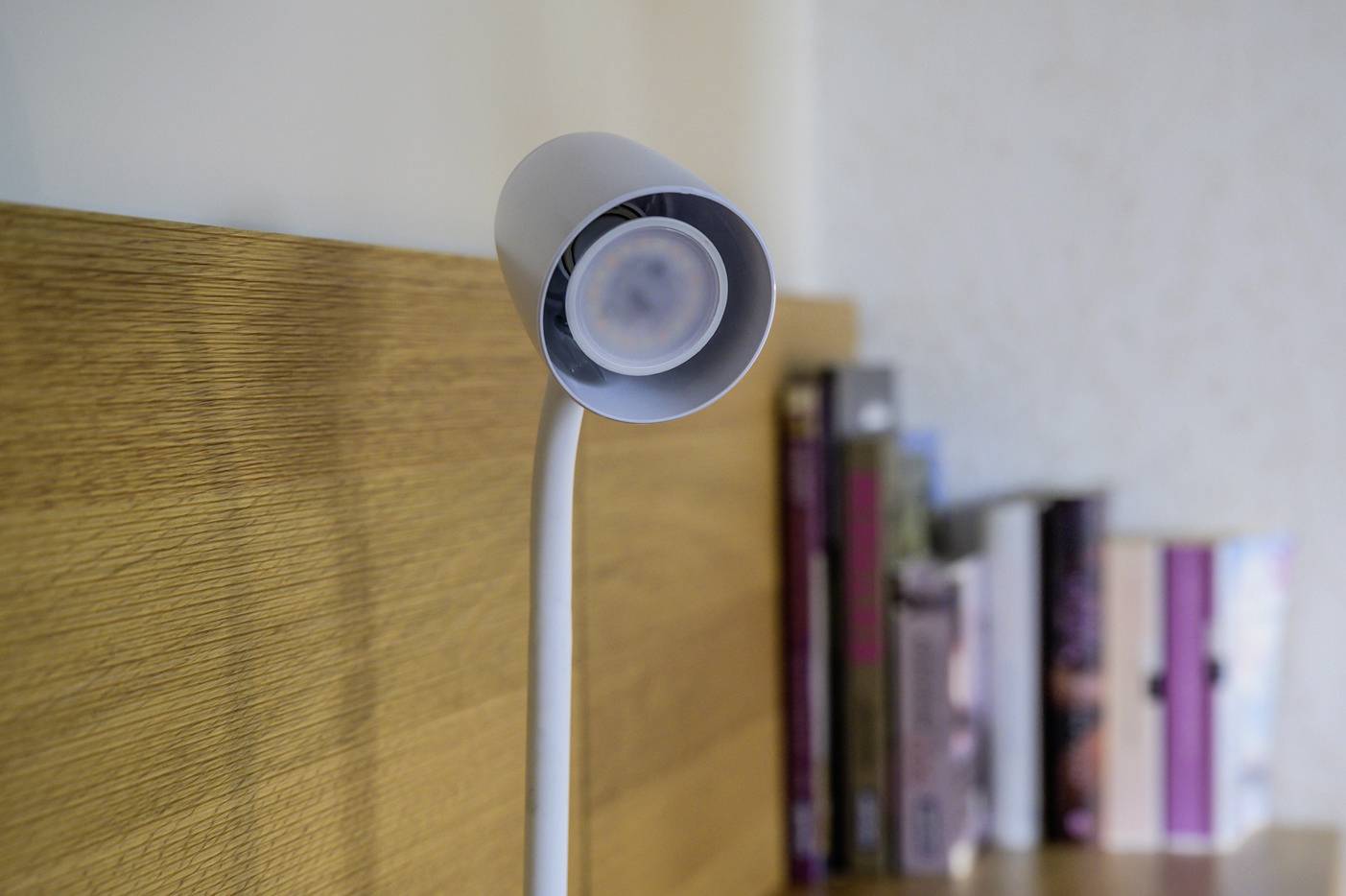 A flexible reading lamp is clamped to a wooden shelf. Some books can be seen blurred in the background.