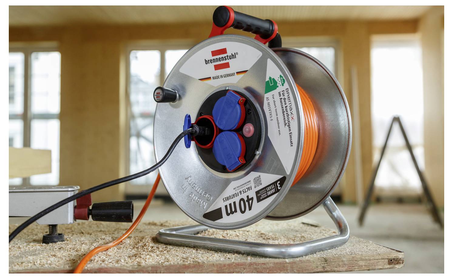 Close-up of a Brennenstuhl 40m cable reel with orange extension cord and blue sockets on a workbench inside a room under construction.