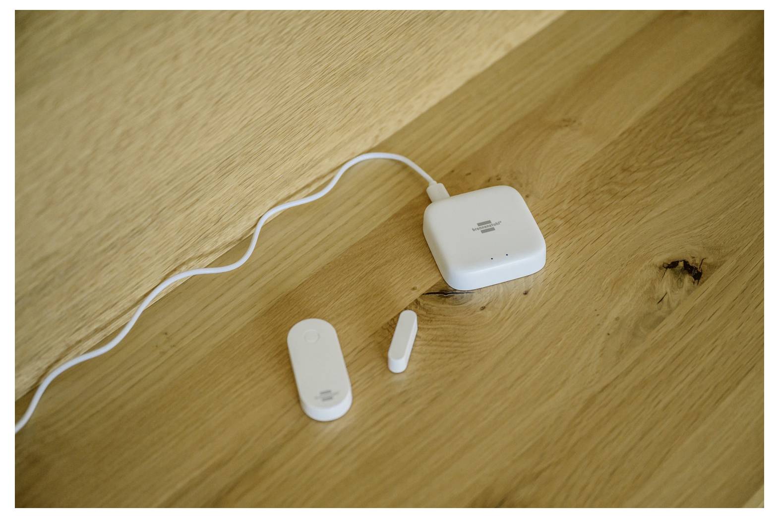 White wireless charging case with a cable on a wooden table, with two small white earbud pieces beside it.
