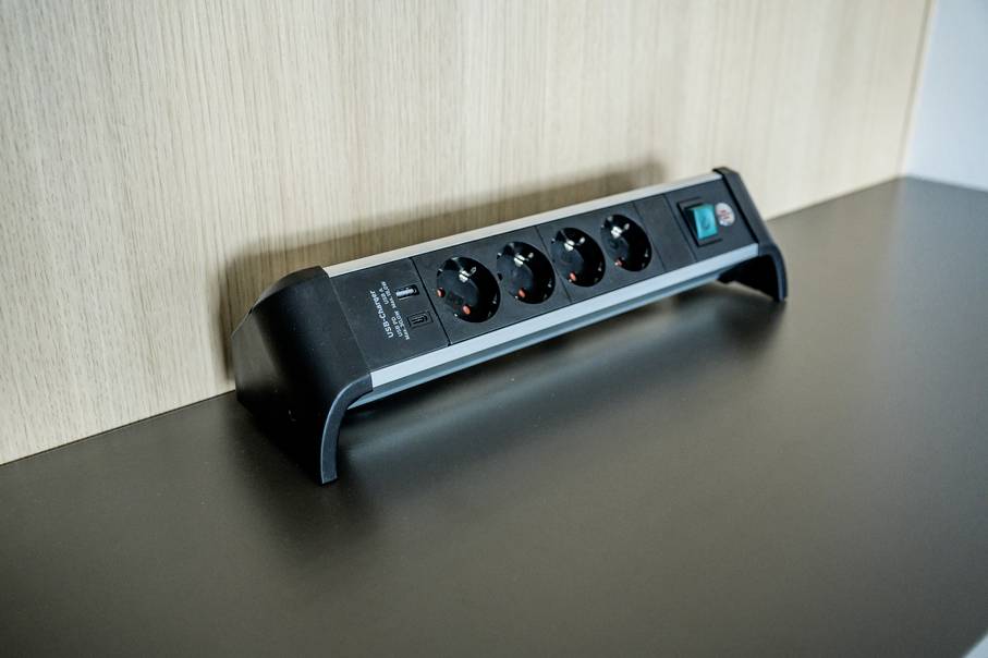 Four-way power strip on a black table, leaning against a wooden wall. Contains a switch on the right side.