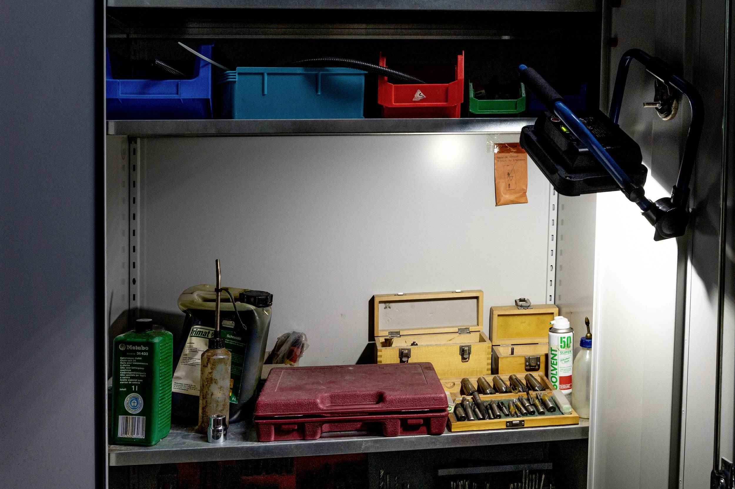 A illuminated metal tool cabinet with various toolboxes, drills, and lubricants. Boxes in blue and red at the top.