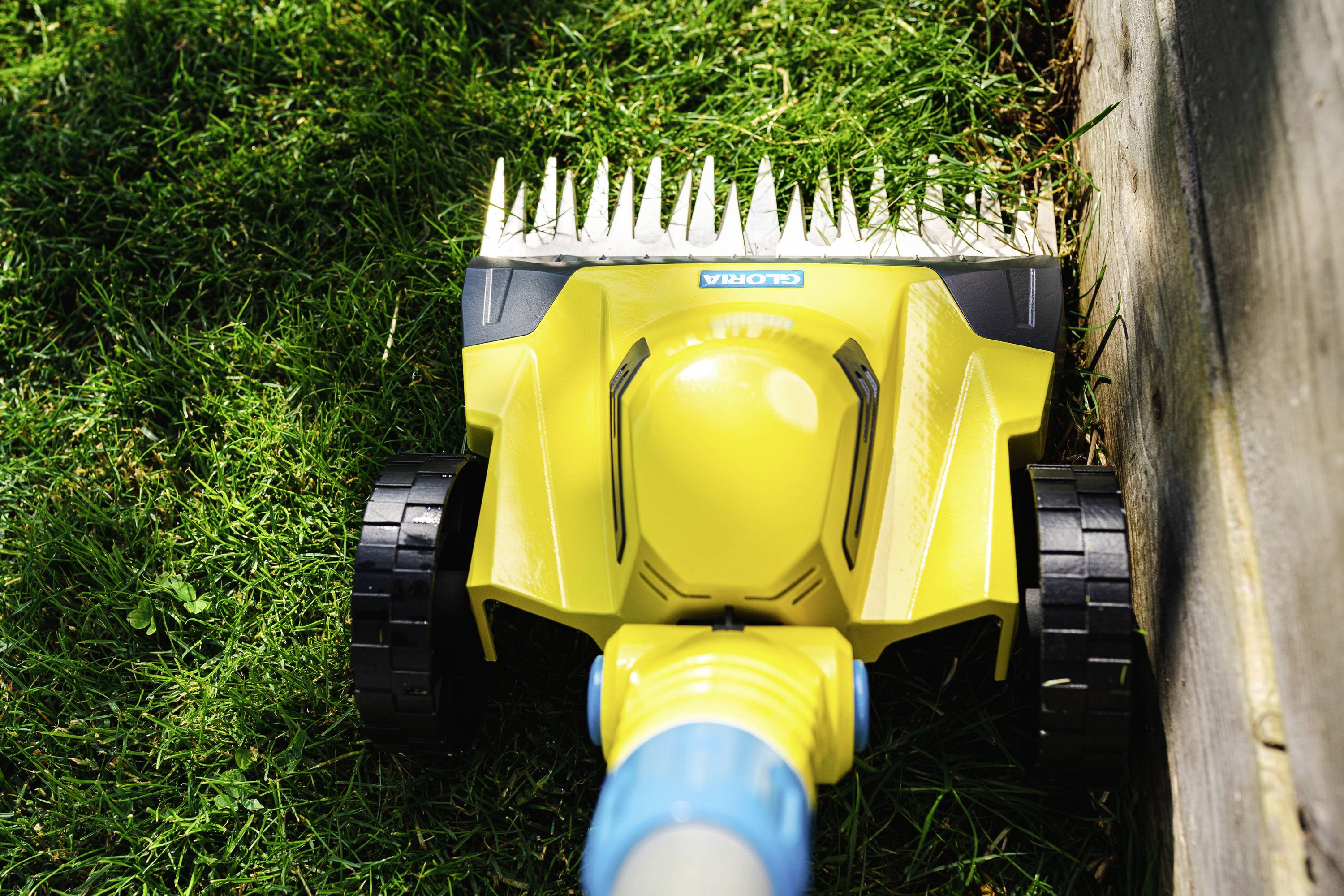 A yellow garden tool cuts grass along a wooden border for neat lawn edges.