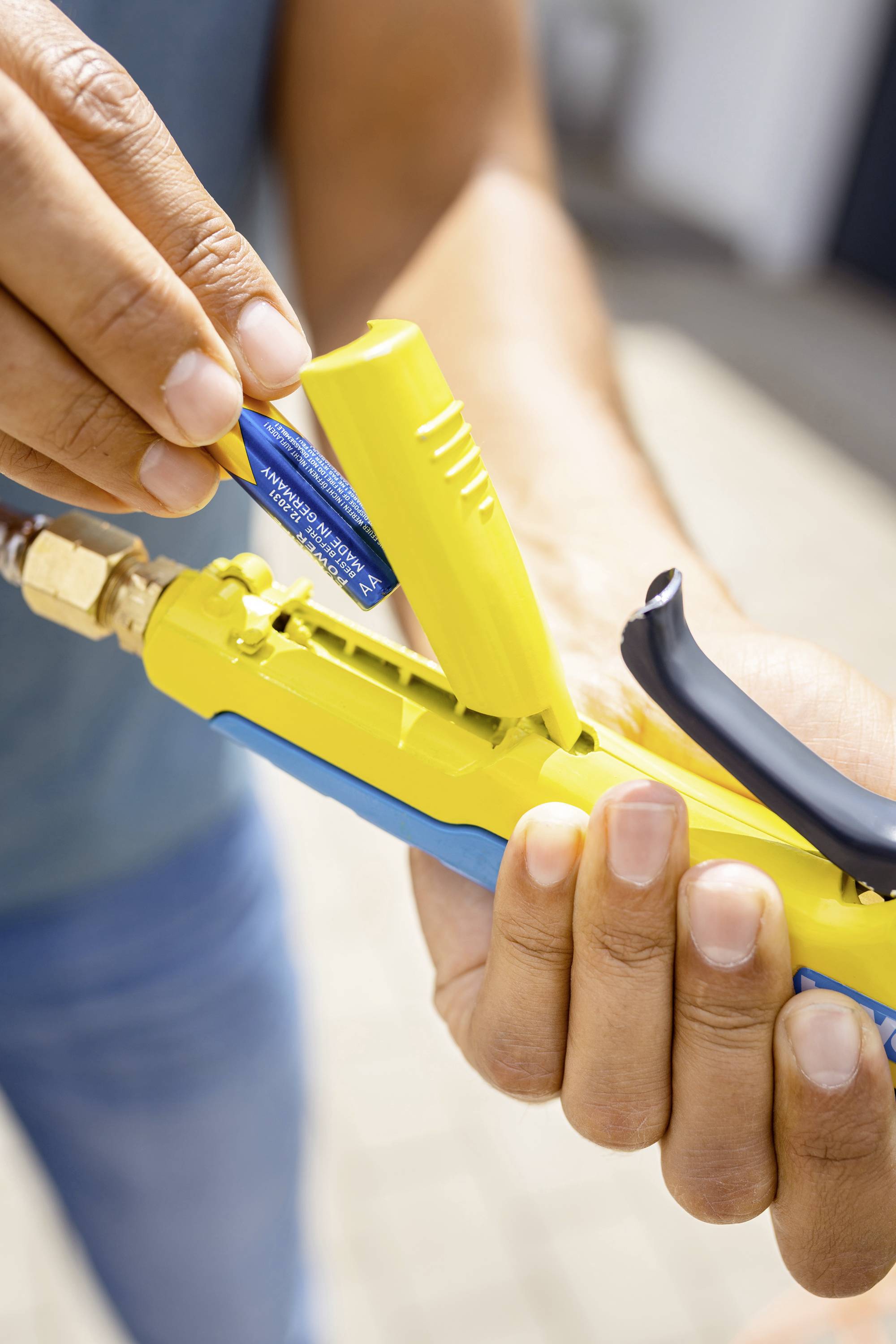 A person is holding a yellow tool and replacing a blue battery, which is likely necessary for the operation of the tool.
