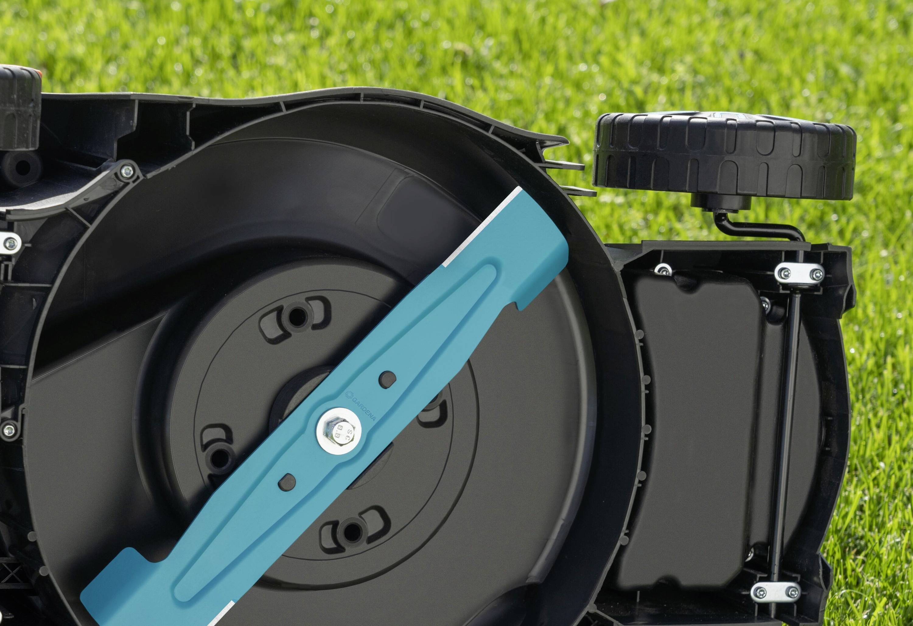 Lawnmower lies on its side, revealing the blue cutting blade. Background: well-maintained, green lawn.