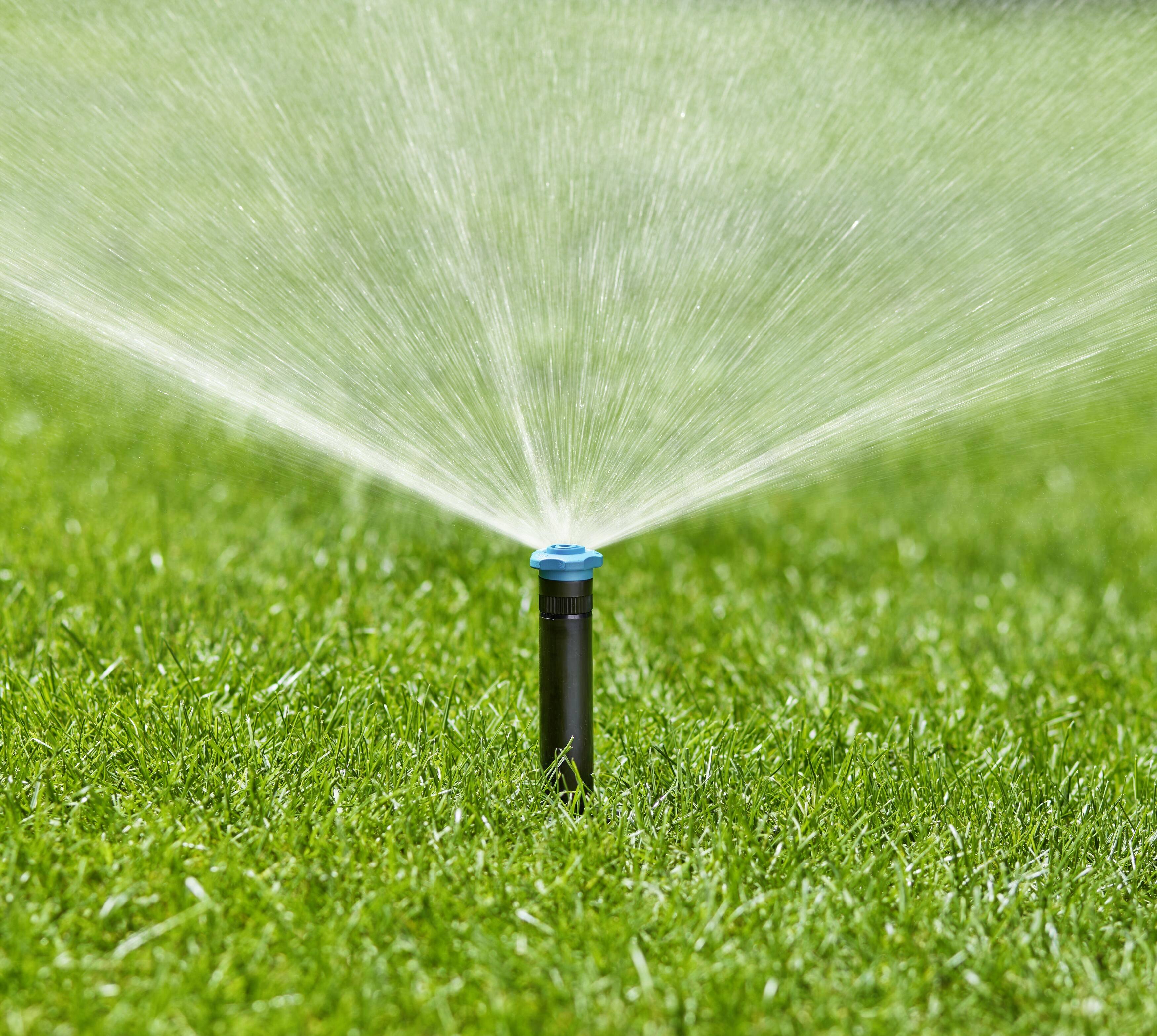 A lawn sprinkler distributes water evenly across green grass to irrigate it.