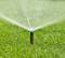 A lawn sprinkler distributes water evenly across green grass to irrigate it.