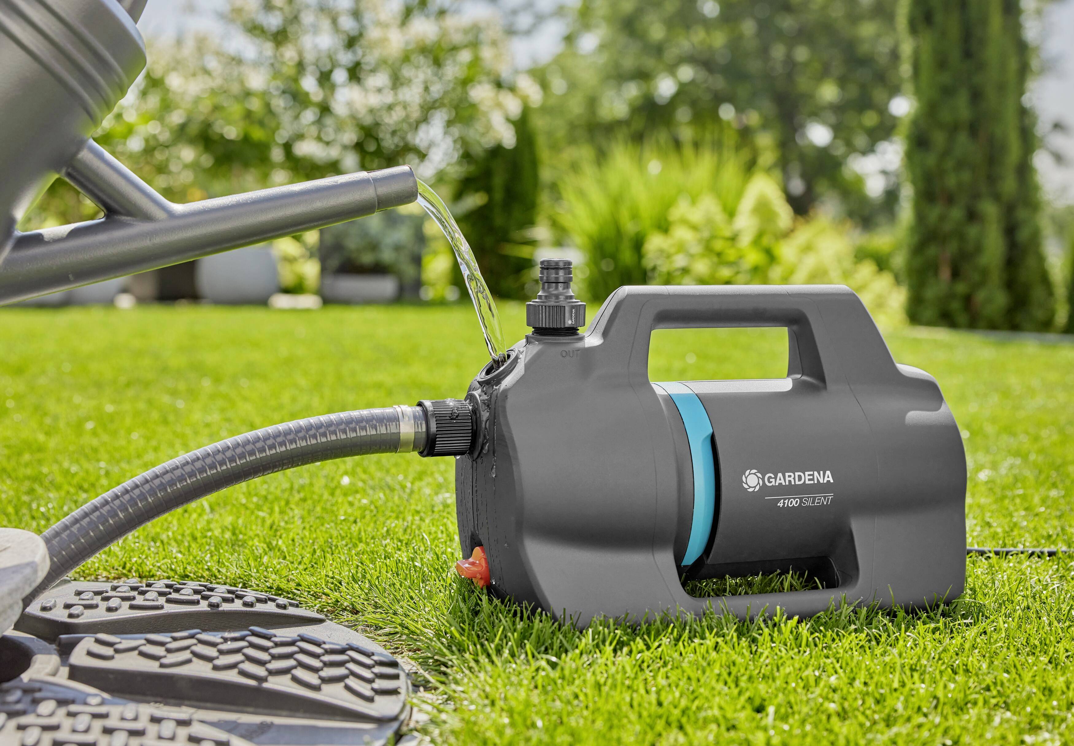 A black water pump on a green lawn is pumping water through a hose. Bushes and trees are visible in the background.