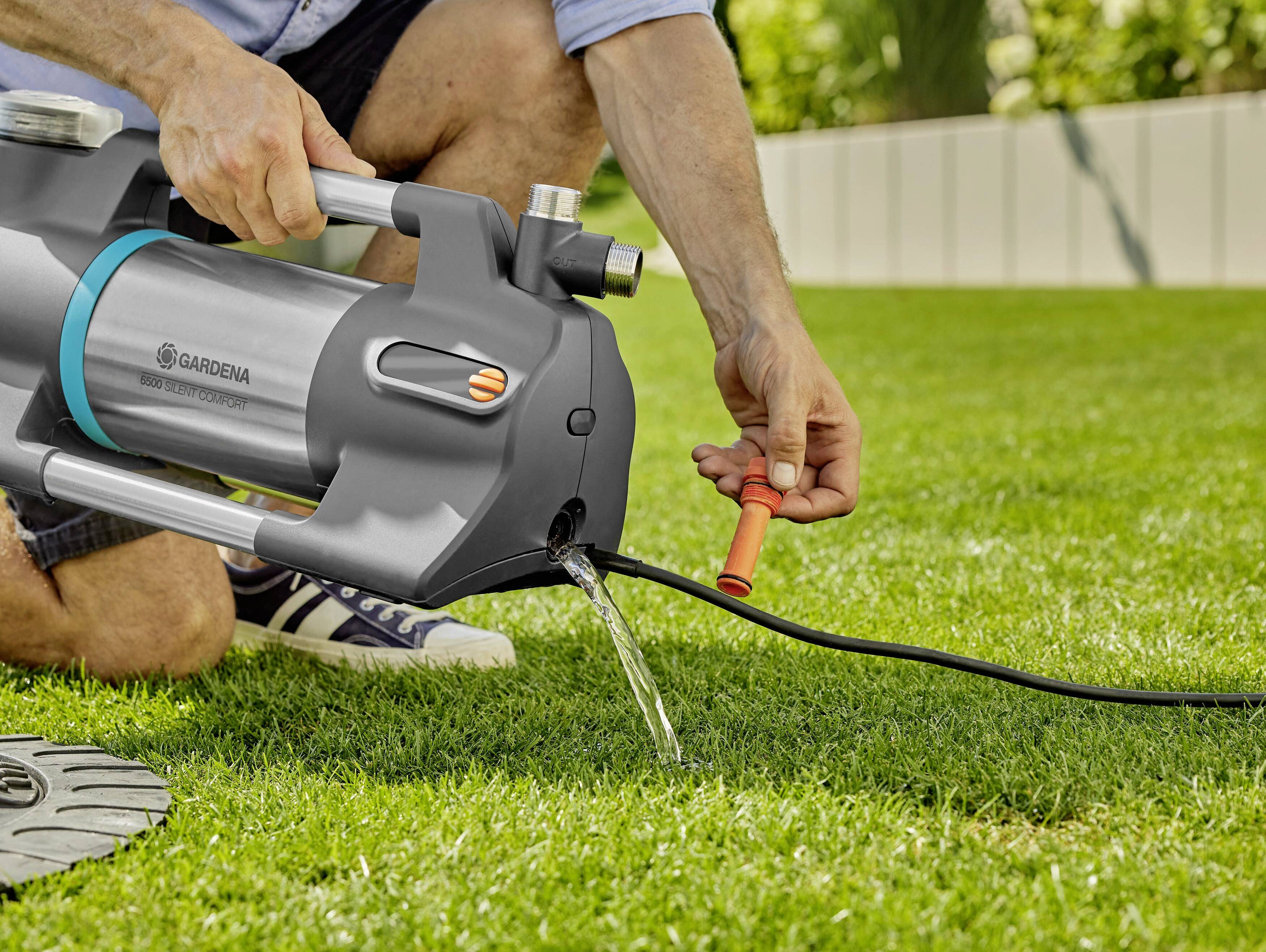 A person is checking a garden pump that is dispersing water onto the lawn.