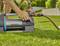 A person is operating a Gardena water pump situated on a green lawn. A hose is connected to the pump.
